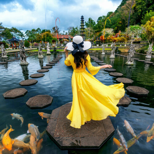 Woman standing in pond with colorful fish at Tirta Gangga Water Palace in Bali, Indonesia.